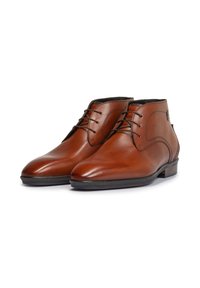 Bruine leren enkelboots met een gladde afwerking, ronde neus, contrasterende stiksels en zwarte veters. Voorzien van een lage gestapelde hak.