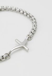 Pulsera de cadena de plata con eslabones redondos y un colgante de cruz pulido. Textura suave con un acabado brillante.