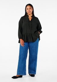 Must värviga peplum-top, millel on V-kaelus ja nöör, millele on paaritatud laiad sinised teksad ja mustad lamedad kingad.