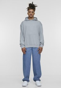 Light gray hooded sweatshirt with a front pocket, paired with blue wide-leg jeans and white sneakers. Smooth fabric and relaxed fit.