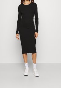 Svart långärmad midiklänning med en figursydd silhuett, tillverkad av mjukt tyg. Vita sneakers med ankellånga strumpor.