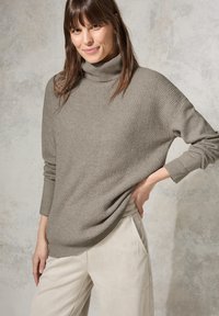 Hellbraunes Rollkragensweatshirt mit gerippter Textur und diagonalem Muster, kombiniert mit cremefarbenen weiten Hosen.