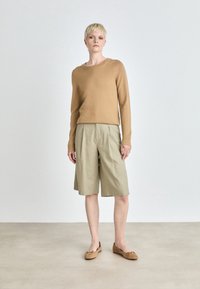 Suéter marrón, pantalones cortos beige a medida y zapatos planos marrón claro. Diseño minimalista con texturas suaves y un corte relajado. Prenda de base bien cuidada.