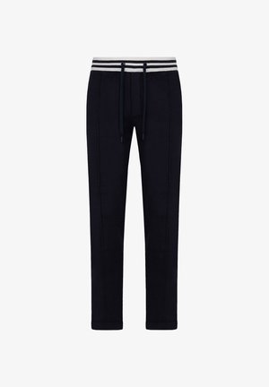 Pantalones de chándal azul marino fabricados en tejido suave, con cintura elástica con cordón, cinturilla a rayas en blanco y gris, y diseño de pierna taperada.
