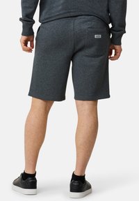 Ciemnoszare szorty dresowe o gładkiej teksturze, z tylną kieszenią i zwężanym krojem; noszone z czarnymi sneakersami i widocznymi skarpetkami na kostki.