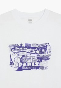 T-shirt blanc avec un collage bleu à thème parisien incluant la Tour Eiffel, des panneaux de métro, l'Arc de Triomphe et des mots comme Paris et Boulangerie.