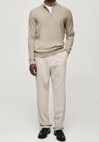 Beżowy sweter z prążkowanej dzianiny z półzamkiem w połączeniu z kremowymi spodniami z kantami. Czarne loafersy dopełniają stylizację. Neutralna paleta kolorów.