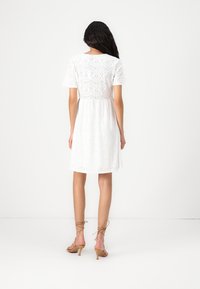 White lace dress with short sleeves, featuring a fitted bodice and flowing skirt. The lace pattern includes cut-out floral designs.