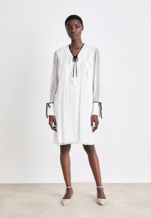 Weißes, knielanges Kleid mit langen, durchsichtigen Ärmeln, Rüschendetails und einer schwarzen Krawattenverschluss am Ausschnitt. Verfügt über schmale Manschetten mit Bändern.