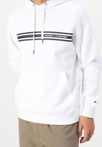 Biała bluza z kapturem z mieszanki bawełny, wyposażona w przednią kieszeń kangura, kaptur ze ściągaczem oraz granatowe paski z logo tekstowym.
