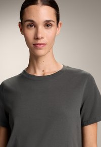 Temno siva bombažna majica s okroglim izrezom in kratkimi rokavi. Mehka tekstura in vidni detajli čistega šivanja. Preprost, minimalističen dizajn.