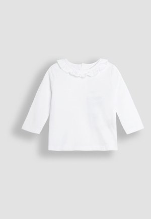 Haut blanc à manches longues en coton, avec un col froncé et une petite fermeture à bouton au dos. Texture lisse sans motifs visibles.