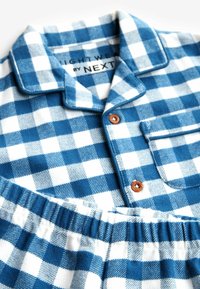 Conjunto de pijama de cuadros azules y blancos, que incluye una parte superior con cuello y botones de madera, además de una cintura elástica en los pantalones, fabricado en un tejido de algodón texturizado.