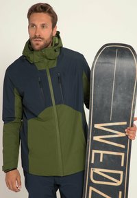 Herres snowboardjakke i grøn og navy, med lynlås fortil, justerbar hætte og flere lynlåslommer. Glat stof med mat tekstur.