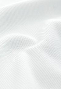 Primer plano de tela blanca suave con finos nervios verticales y pliegues suaves que muestran la textura y las sombras ligeras.