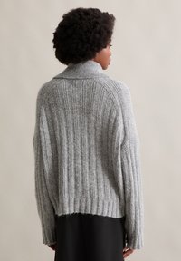 Szary sweter z dzianiny o wysokim kołnierzu, z pionowym prążkowanym wzorem i lekko skróconym krojem, w kontraście z czarnymi spodniami.