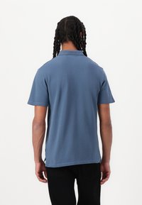 Πολο μπλούζα σε ανοιχτό μπλε ύφασμα, κοντά μανίκια, κλασικό γιακά, χωρίς ραφές στους ώμους, προσαρμοσμένη εφαρμογή, όψη από πίσω, λεπτομέρεια ραφής διακριτική.