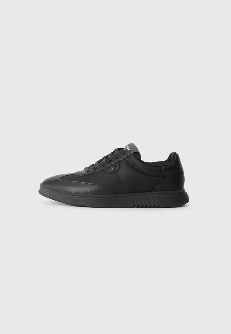 Black low-top sneaker made of smooth leather with rounded toe, lace-up front, textured sole, and subtle branding on the side.