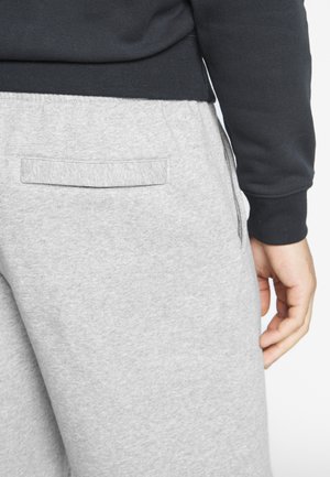 Graue Baumwoll-Jogginghose mit einer Gesäßtasche, kombiniert mit einem schwarzen Langarmshirt. Der Stoff wirkt weich und hat eine glatte Textur.