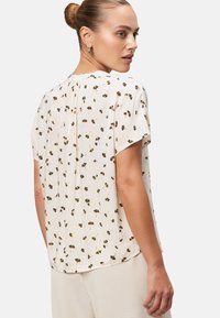 Korte mouwen blouse in lichtcrème met een bloemenprint. Heeft een geplooide achterkant en een ontspannen pasvorm. Gemaakt van lichte, gladde stof.