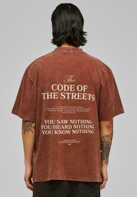 Camiseta oversize marrón con texto blanco en la parte posterior, con un acabado vintage y mangas cortas. El diseño incluye citas sobre el respeto.