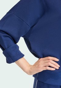 Svetrová mikina námorníckej modrej farby s ribovanými manžetami. Má voľný strih a mäkkú, textúrovanú látku. Obsahuje prešívané švy a okrúhly výstrih.