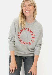Grijze sweatshirt met rode ronde tekst "HOME SWEET EARTH." Ribgebreide boorden en halslijn. Gecombineerd met donkergrijze jeans.