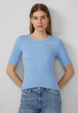 Camiseta ajustada de color azul claro, hecha de tejido acanalado, con mangas cortas y cuello redondo. Combinada con unos vaqueros azules.