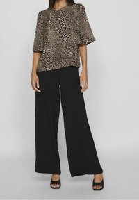 Top a stampa leopardata beige e nera con maniche corte, abbinato a pantaloni neri a gamba larga e tacchi aperti neri. Tessuto dal tocco morbido.