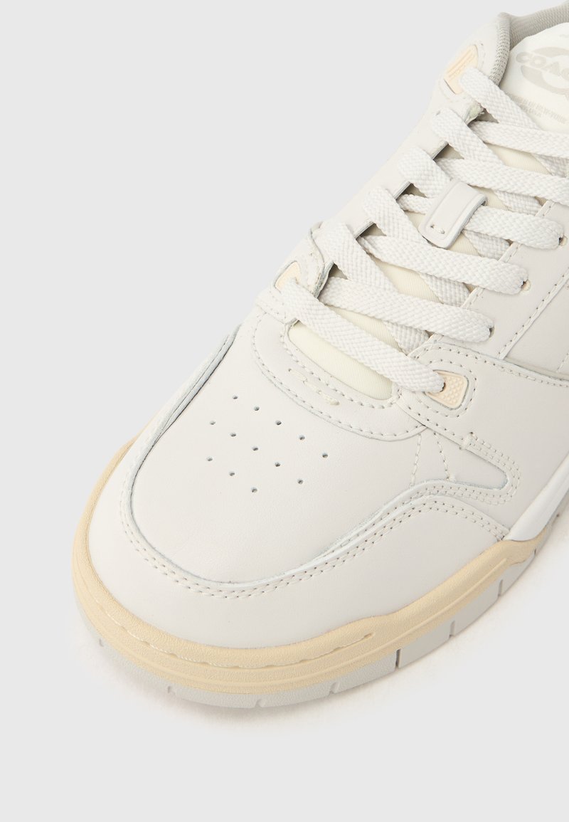 White leather sneaker with a smooth finish, round toe, perforated detailing, cream laces, and a light beige rubber sole.