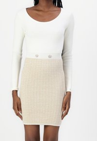 Robe en tricot avec un haut blanc et un bas beige texturé, accentuée par deux boutons décoratifs à la taille.