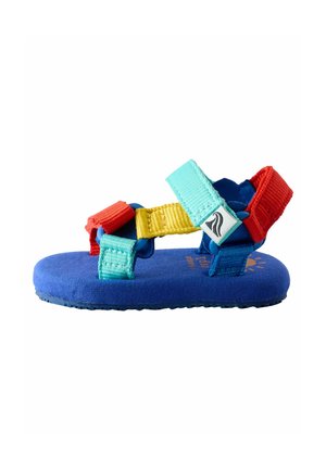 Krāsains sandals ar zilu zoli ar teksturētu virsmu, nostiprināts ar regulējamiem siksniņām sarkanā, dzeltenā un tirkīza krāsā.