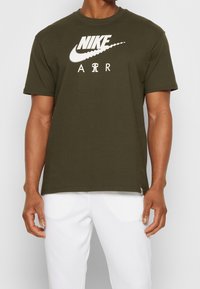 Olivově zelené bavlněné tričko s krátkým rukávem, s velkým bílým logem Nike a textem "AIR" v tučném, moderním písmu.