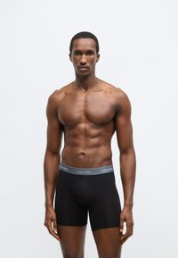 Boxeri negri cu o talie gri Calvin Klein, având o potrivire strânsă și o textură netedă, prezentați pe un model masculin fără tricou.