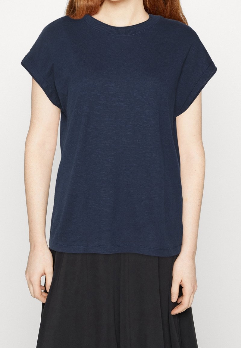 Femme portant un t-shirt ample à manches courtes bleu marine associé à une jupe noire, vue du cou jusqu'aux hanches.