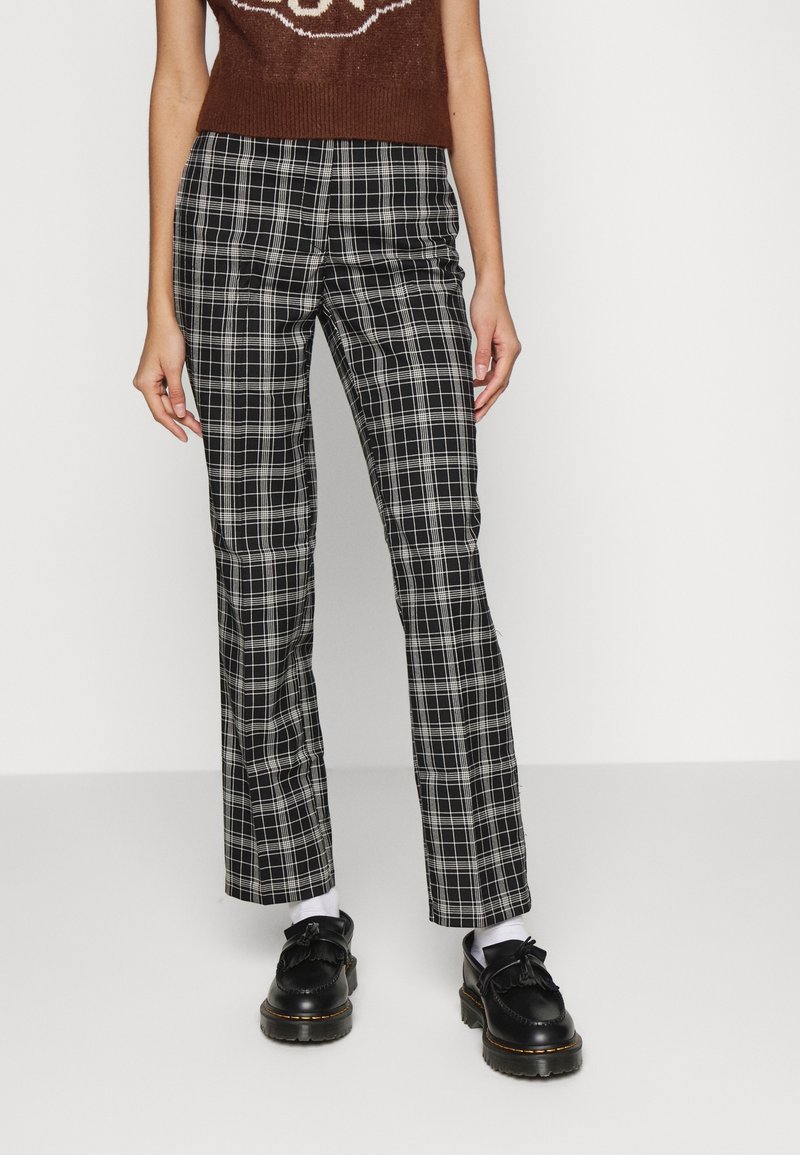 Pantalon à carreaux noir et blanc à coupe droite, en tissu tissé. Le design présente un motif à carreaux et des poches latérales. Des chaussures noires complètent le look.