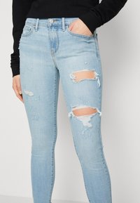 Jeans skinny de mezclilla azul claro con detalles desgastados y rotos en las rodillas. Presenta un cierre de botón y bolsillos frontales.