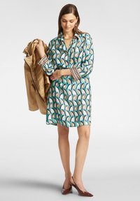 Abito a maniche corte con un motivo geometrico nei toni del blu, verde e beige. Tessuto leggero e lunghezza sopra il ginocchio, abbinato a un giacca beige.