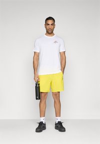 White short-sleeve shirt with a red logo, yellow shorts, black water bottle, black sneakers, and white socks. Simple athletic design.