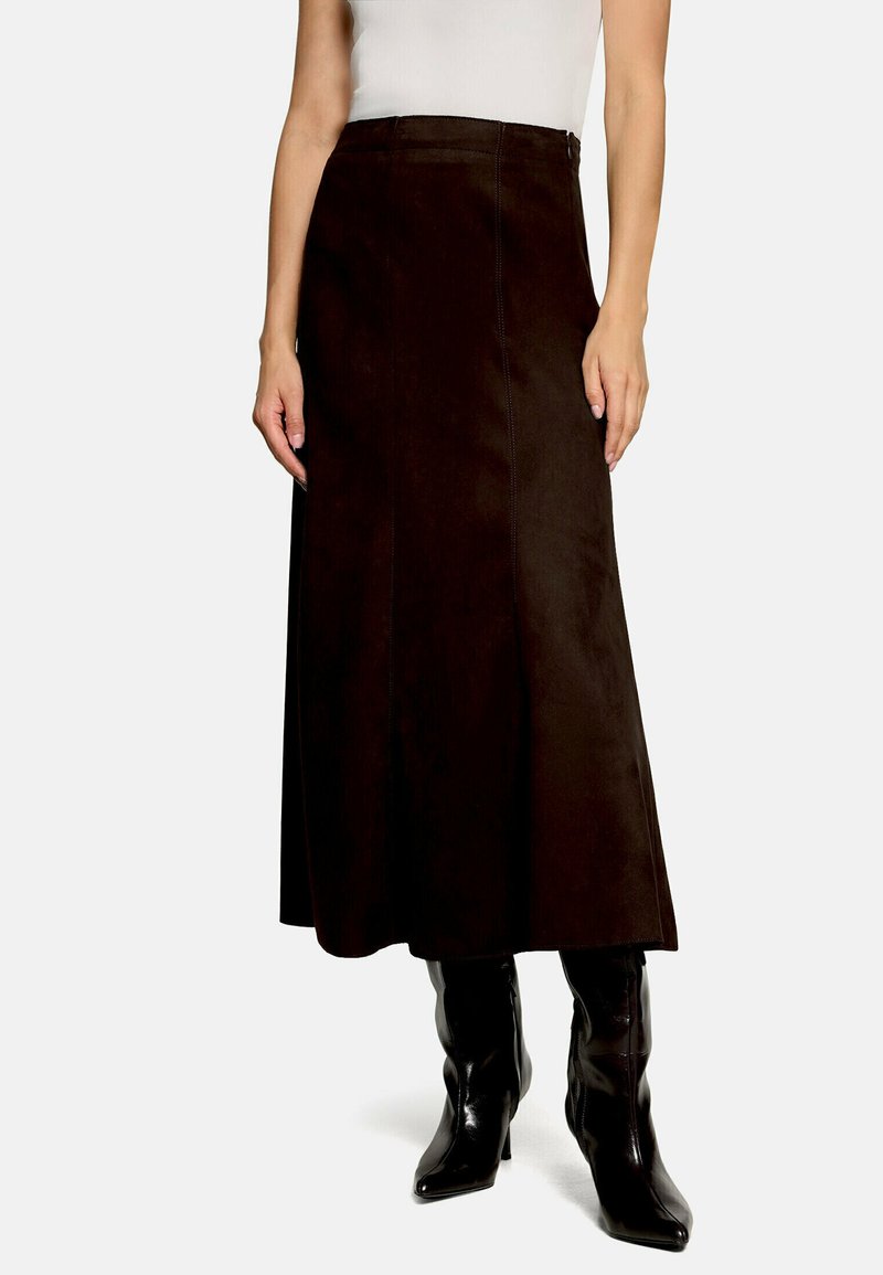 Femme portant une jupe midi noire taille haute en coupe trapèze, un top blanc sans manches ajusté et des bottines noires à talons.
