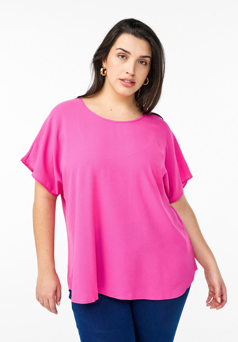 Roze oversized top met korte, brede mouwen en een ronde halslijn. Lichtgewicht stof met een gladde textuur, gecombineerd met donkerblauwe broek.