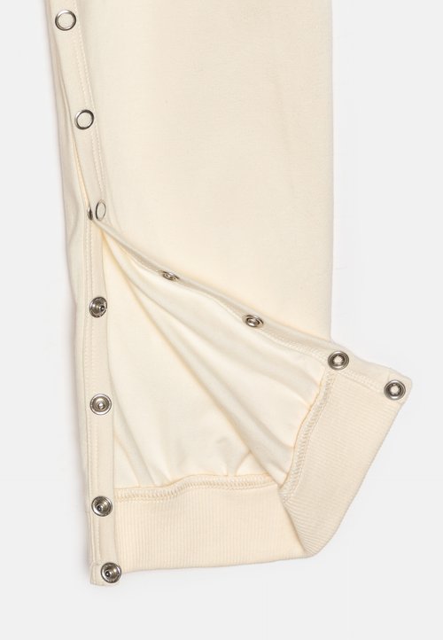 Poignet en tissu crème avec des boutons-pression en argent sur le côté, présentant une texture côtelée à l'ourlet et une surface lisse dans l'ensemble.