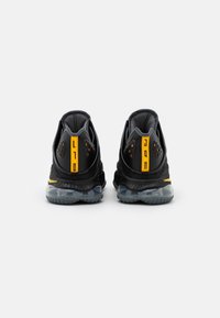 Sneakers sportivi neri con una tomaia strutturata, accenti gialli e suola trasparente. Caratteristiche includono pannelli in mesh e design perforato.