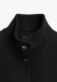 Black wool blend coat featuring a high collar, two black buttons, and a textured finish. Simple design with clean lines.