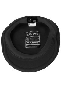 Cappello in lana nero Kangol girato al rovescio che mostra l'etichetta di taglia media e le istruzioni di cura con i simboli di lavaggio e il testo "Progettato in Gran Bretagna".