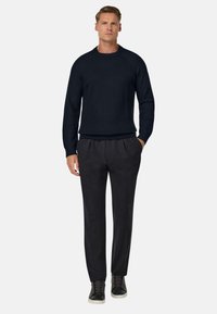 Donkerblauwe geribbelde gebreide trui met lange mouwen, gecombineerd met zwarte taps toelopende broek en donkere sneakers, wat een casual, slim fit ontwerp benadrukt.