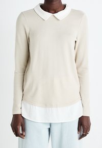 Crèmekleurige top met lange mouwen en een witte kraag, zachte textuur, afgeronde zoom, gelaagd ontwerp over een wit shirt en een losse pasvorm.