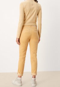 Pantaloni gialli in corduroy con taglio dritto, orli arrotolati e una trama liscia, abbinati a sneakers grigio chiaro e un top beige a coste.