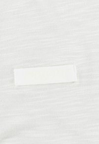 Biały materiał o subtelnym wzorze teksturowanym, z białą etykietą z wytłoczonym napisem "PRD". Materiał wydaje się lekki i gładki.