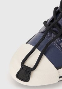 Navy leather sneaker with a white rubber toe cap, black laces, and a small black lace tag. Textured upper with contrasting design elements.